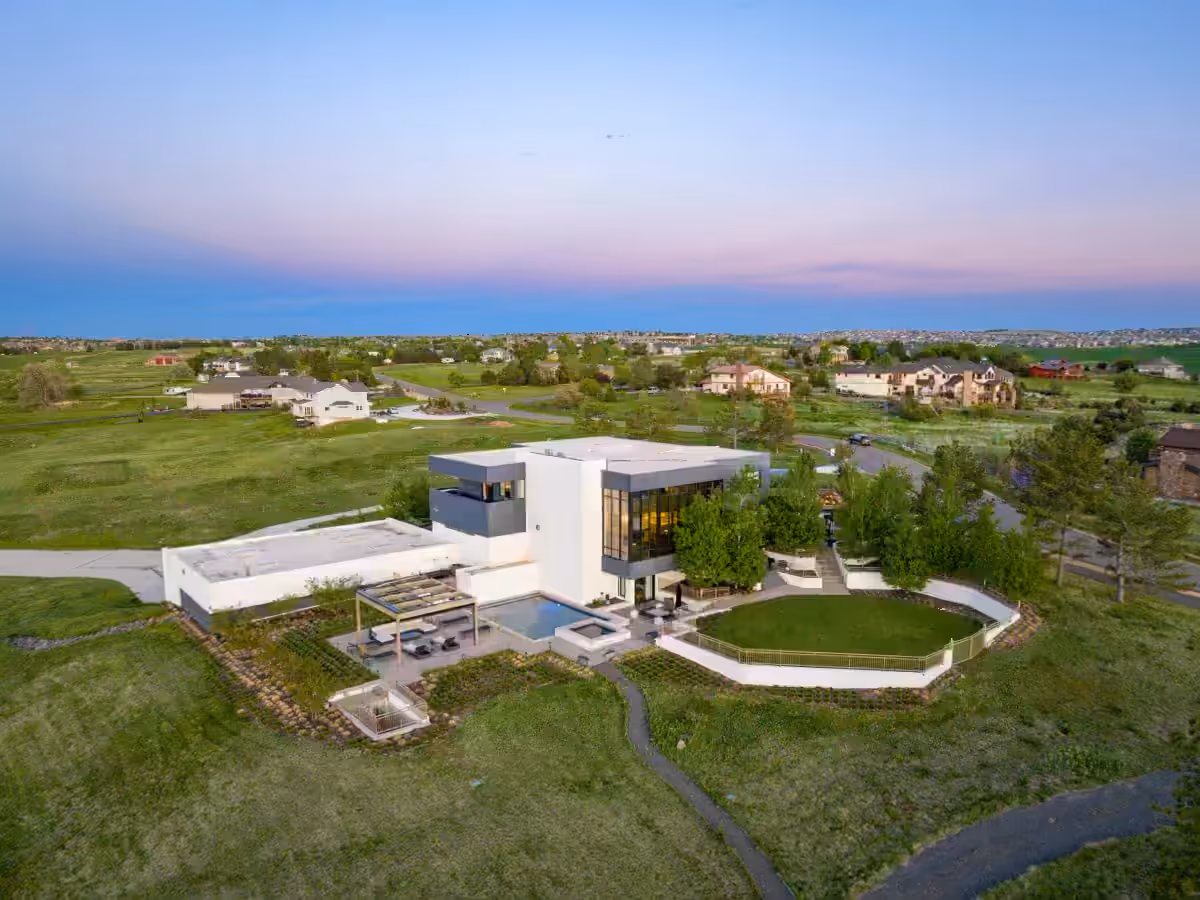 A contemporary flat-roofed residence at dusk seen from the air, with a pool terrace, lawn and the plains of the Front Range beyond.
