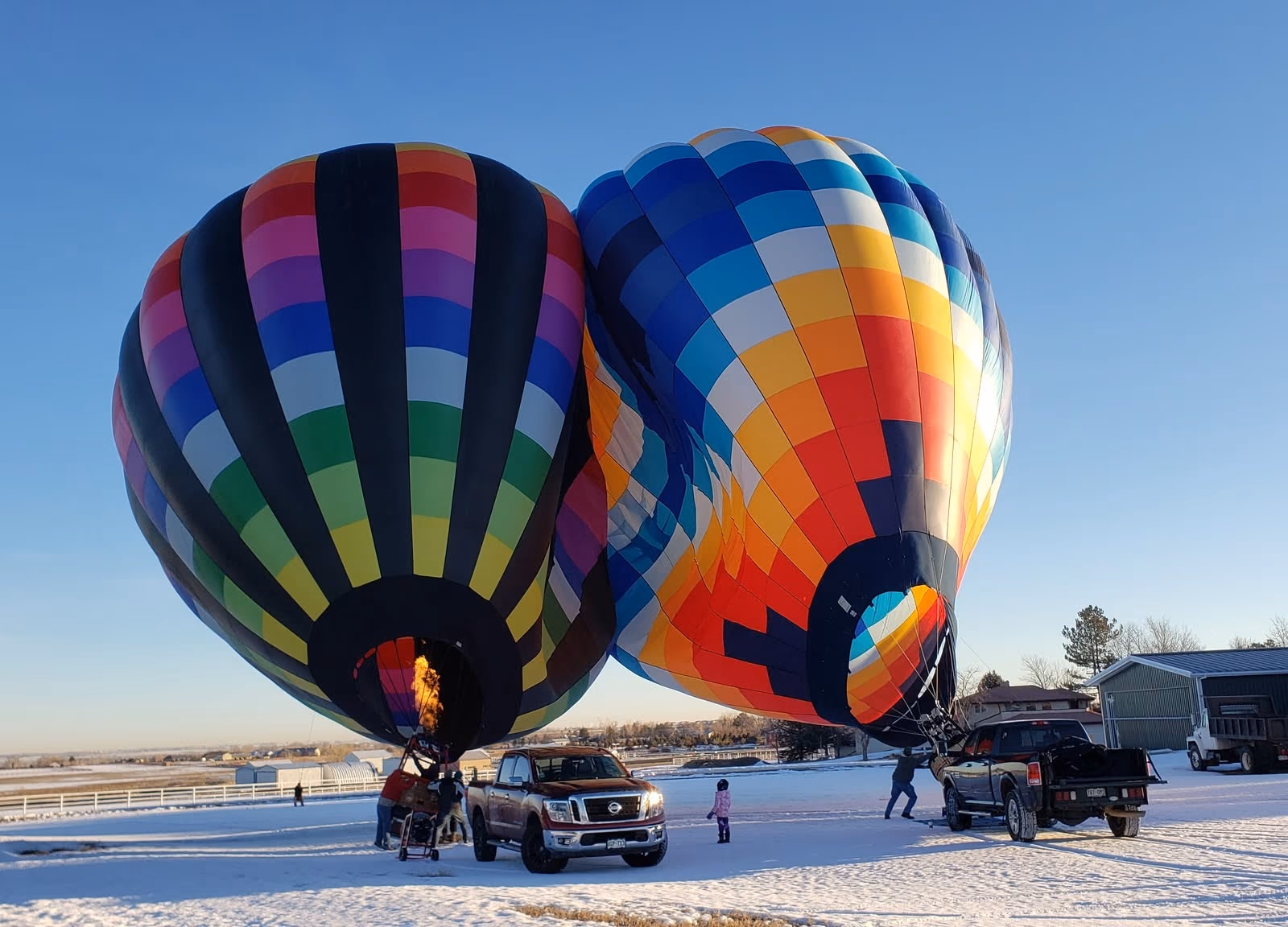 Two hot-air balloons inflating on snowy ground with Parkland Estates homes behind.