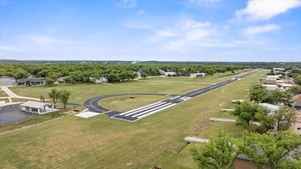 A residential airpark runway with displaced threshold markings and a segmented circle, homes and hangars along both sides.