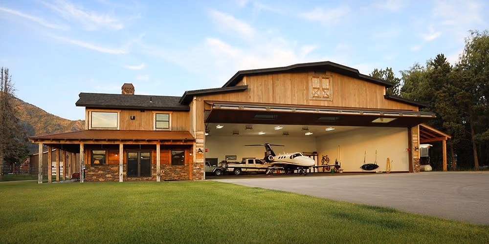 A barn-style hangar home with the bifold door open and a light jet parked inside.
