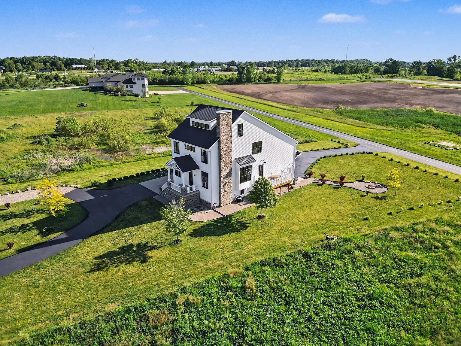 An aerial view of a white farmhouse hangar home on open acreage.