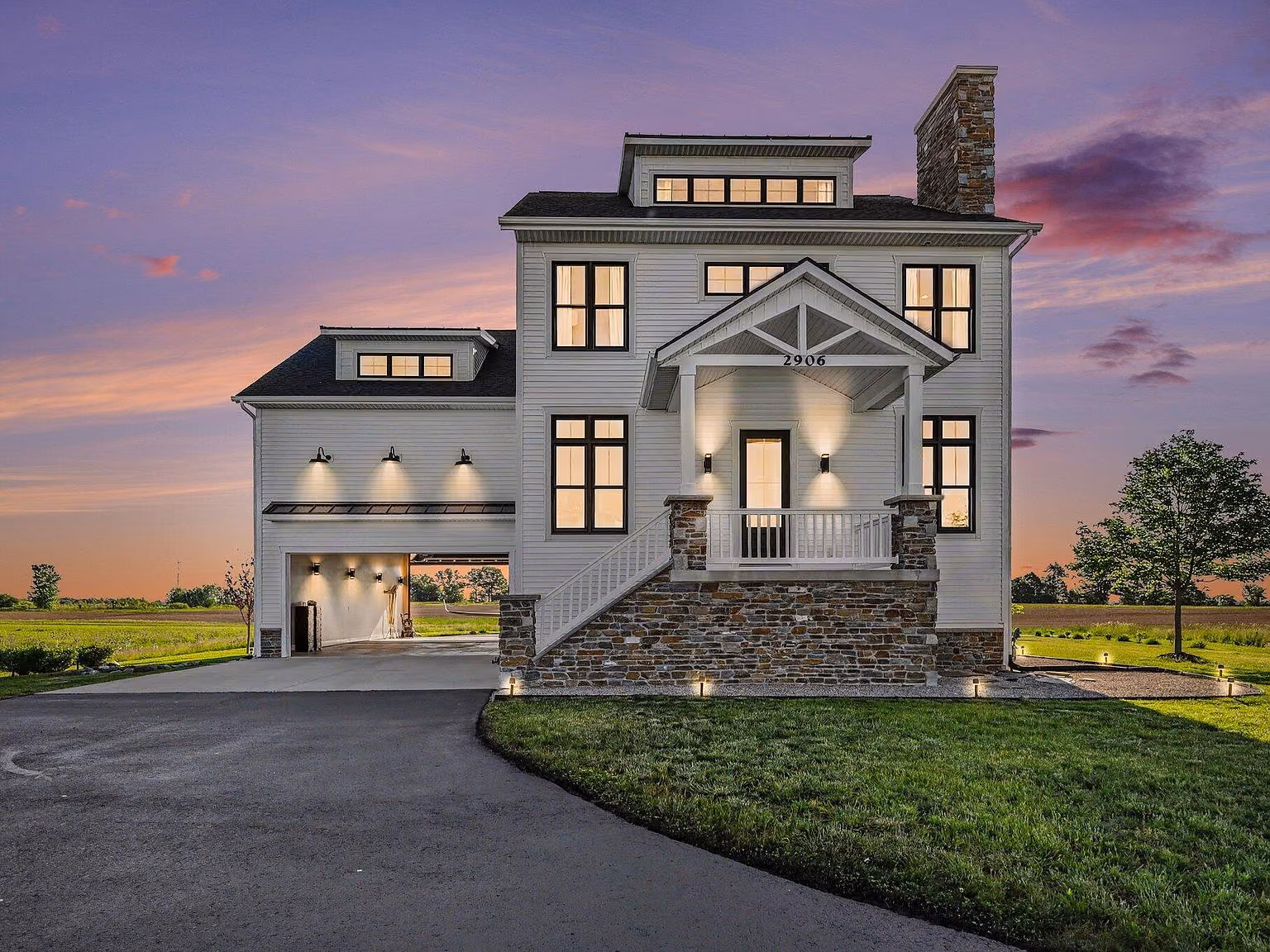 A white modern farmhouse hangar home with a stone chimney on green acreage.