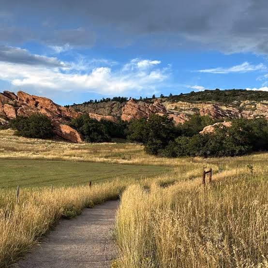 A walking path through tall grass toward red rock outcrops in evening light.