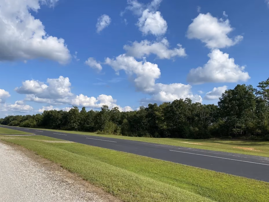A paved airpark runway edged by mown grass and a tree line.