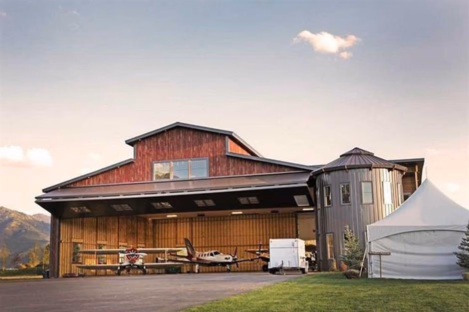 A red barn-style hangar with a silo stair tower and two aircraft under the open bifold door.
