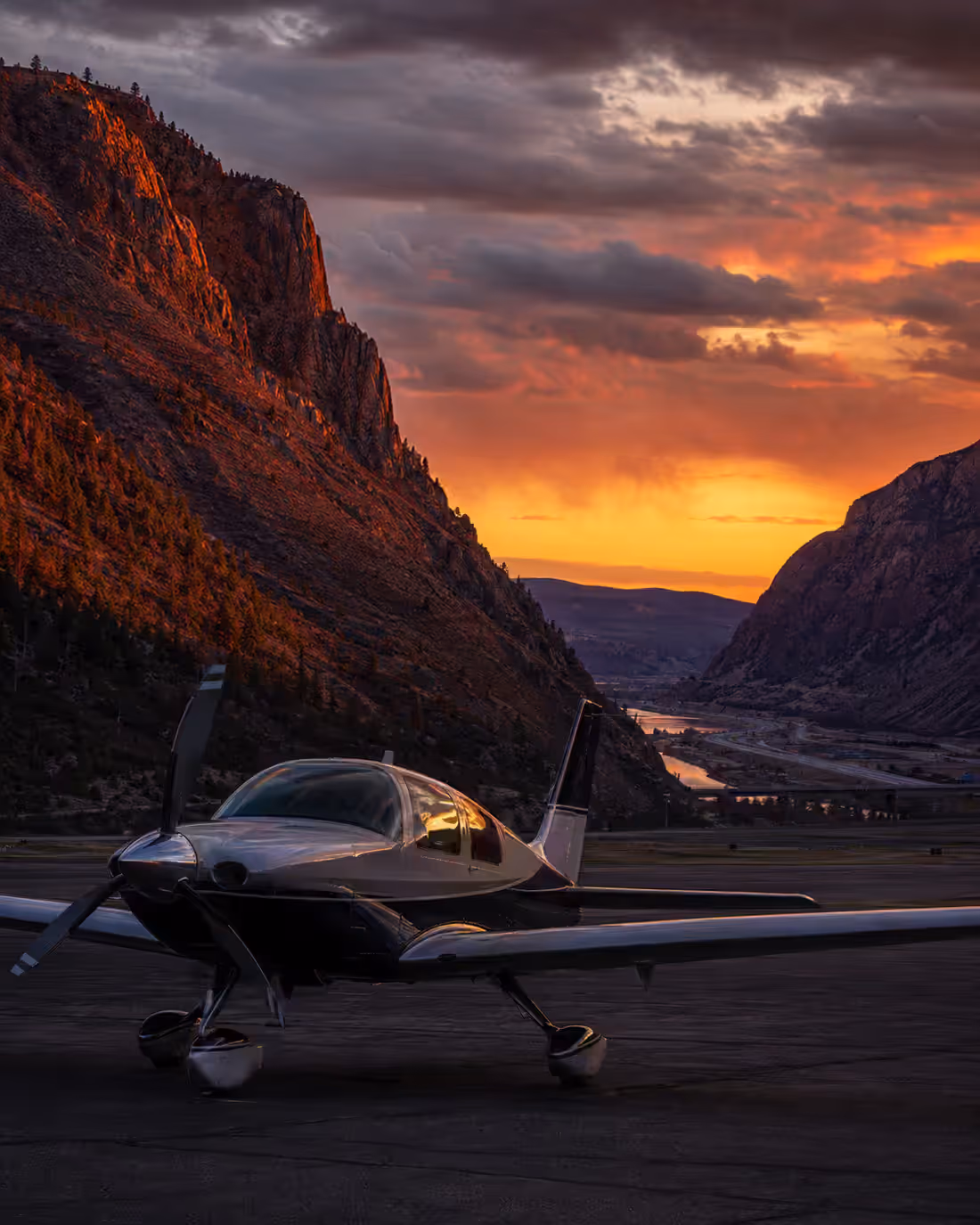 A composite single parked on a canyon airstrip at sunset, the cliff wall above it lit red