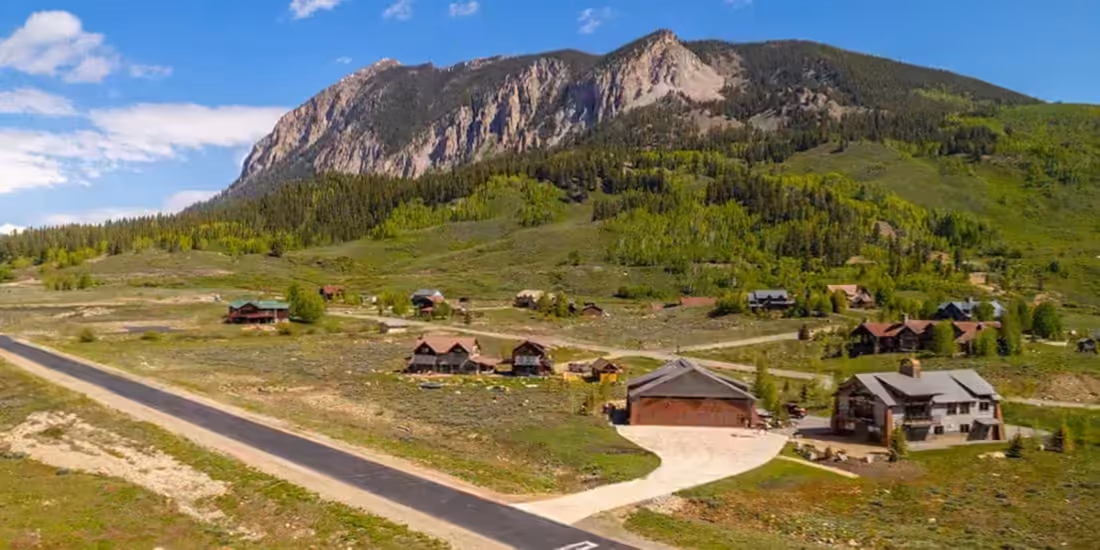 A wide view along an airpark runway, homes and hangars set back along its length beneath a mountain