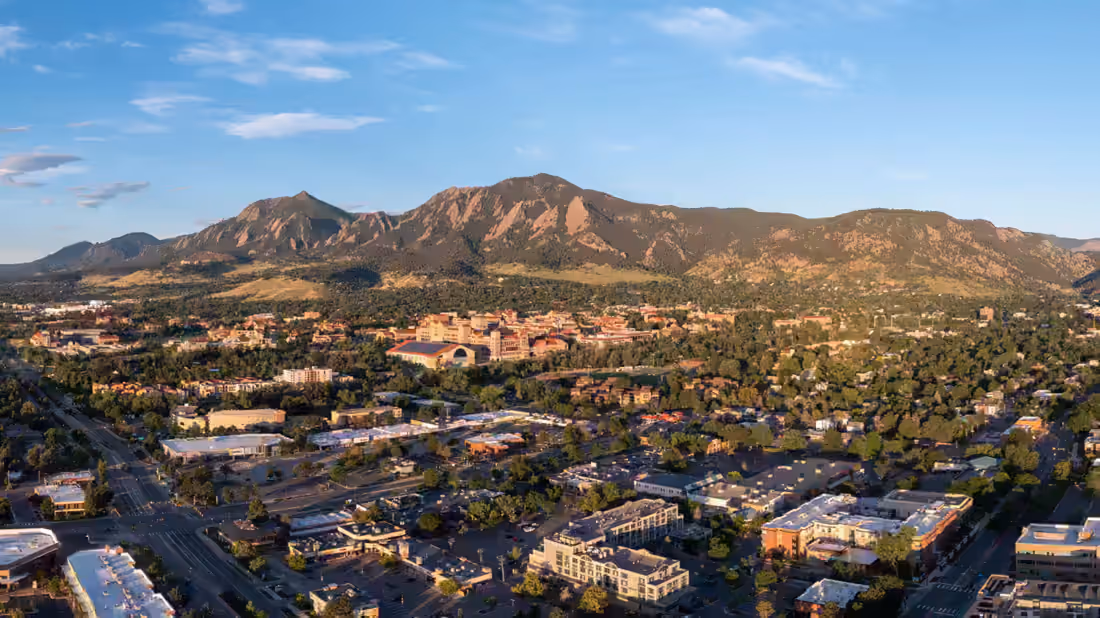 Boulder from the air at golden hour, the Flatirons behind and the university campus in the middle distance