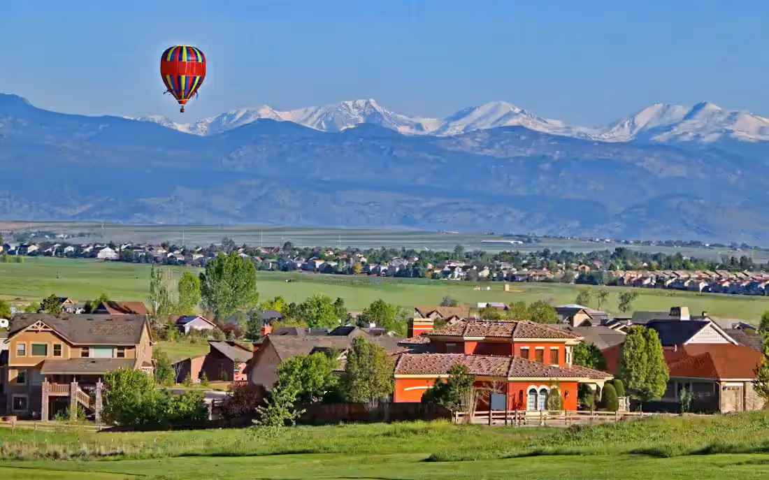 A balloon over plains rooftops with the snow-covered Front Range behind