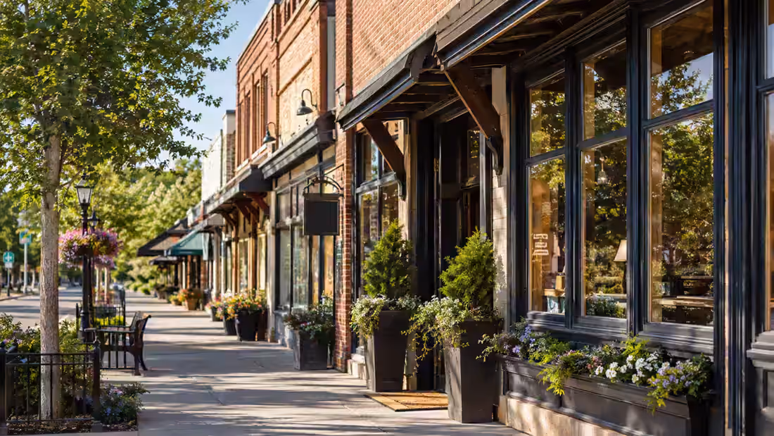Brick storefronts along a swept sidewalk, awnings and window boxes, a bench under a street tree