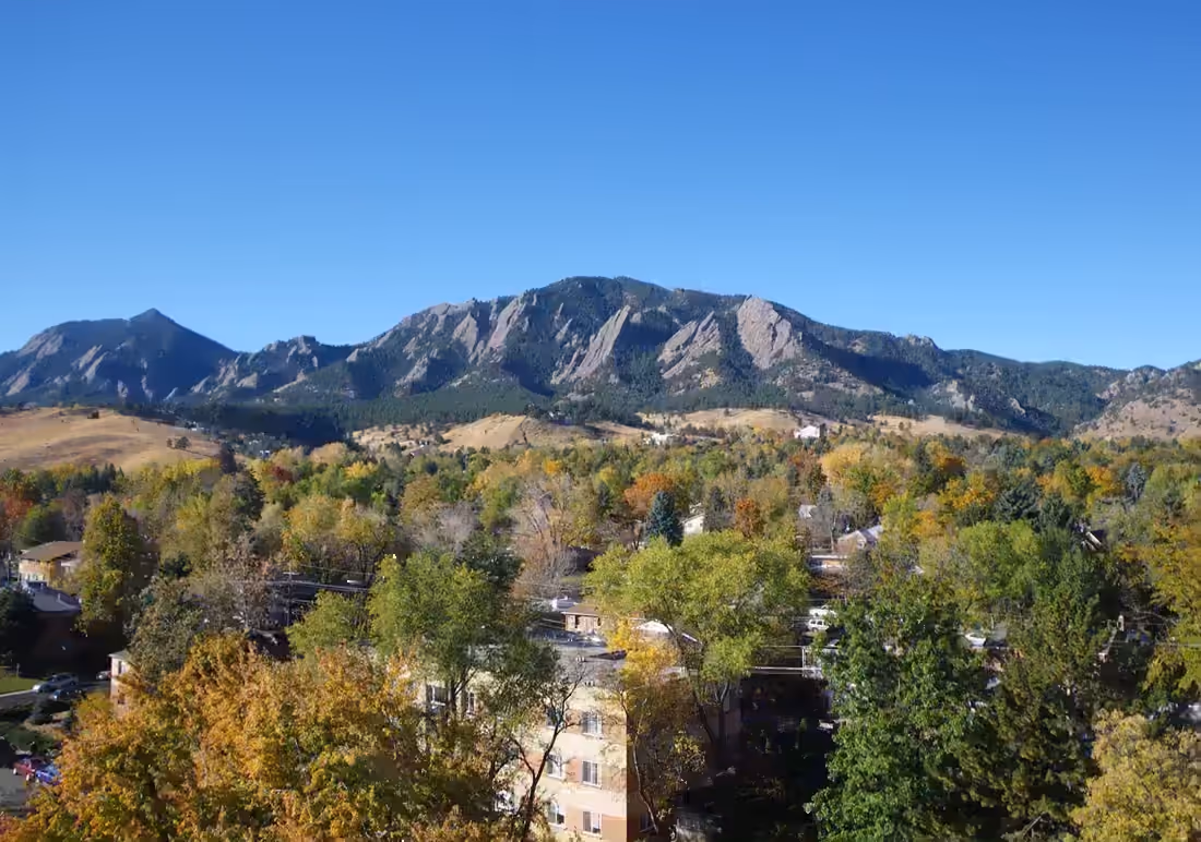 The Flatirons rising over an autumn tree canopy and rooftops