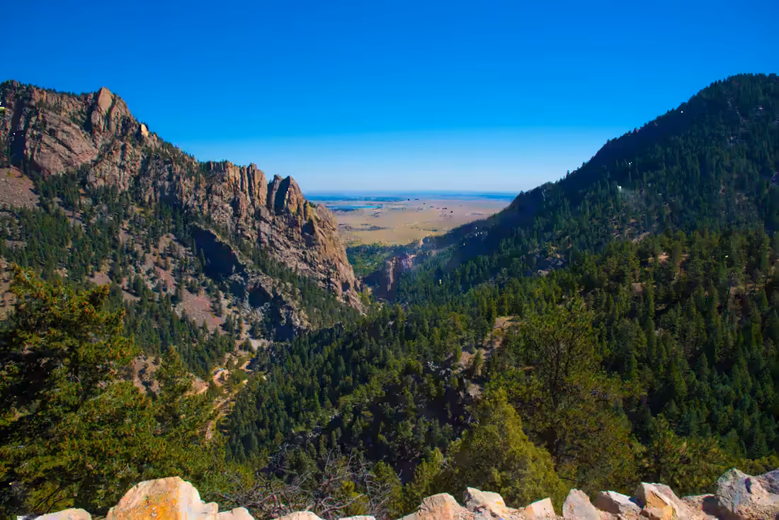 A foothills canyon looking east, granite outcrops above forested slopes and the plains beyond