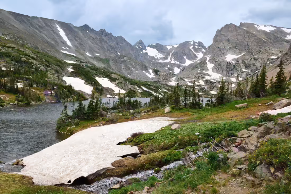 An alpine lake and a lingering snowfield below the jagged Indian Peaks