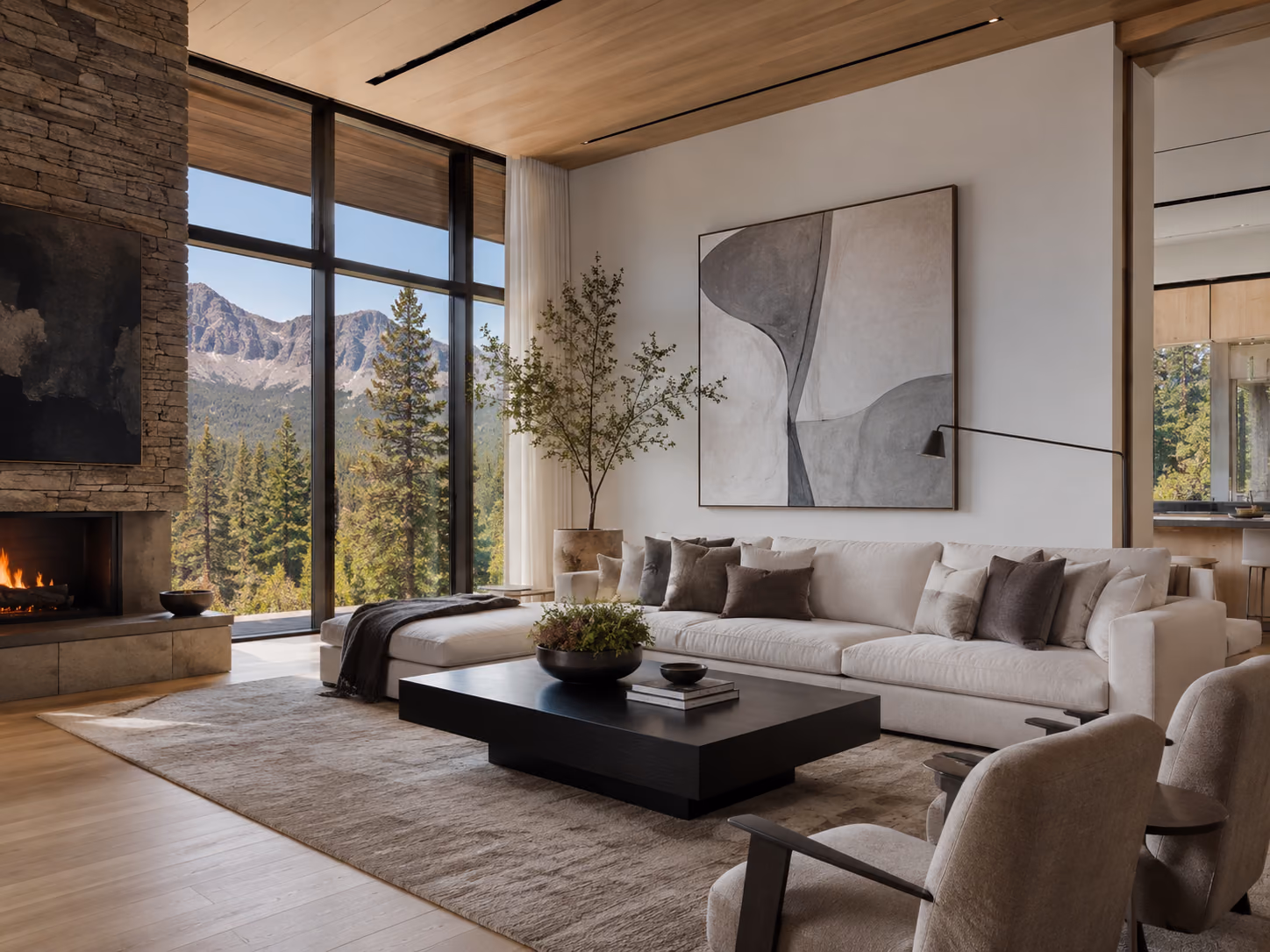 Living room anchored by a floor-to-ceiling stacked-stone fireplace, with a cream sectional and a window wall looking out to conifers and a rock summit
