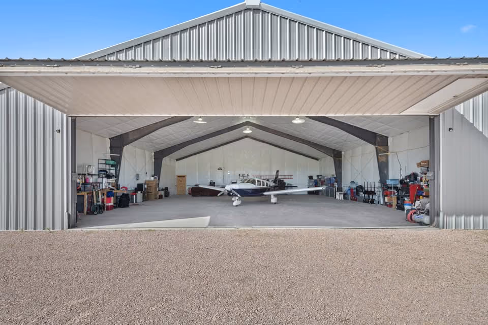 A wide steel hangar at Kelly Air Park with a low-wing aircraft parked inside.
