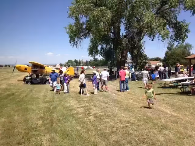 Residents gathered on the grass beside a yellow taildragger at a Van Aire community event.